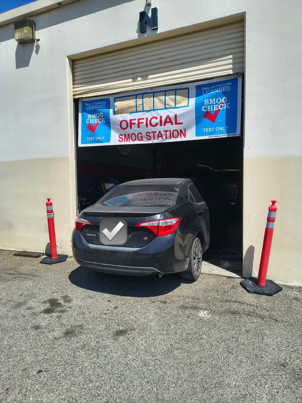 Black Toyota Corolla backing into the smog test bay between orange safety posts
