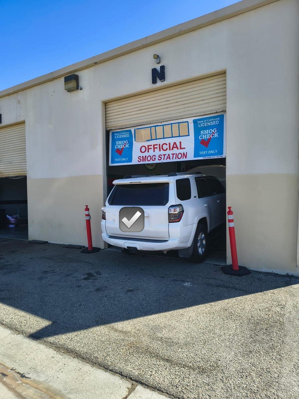 White Toyota 4Runner pulling into roll-up bay N under the Official Smog Station banner