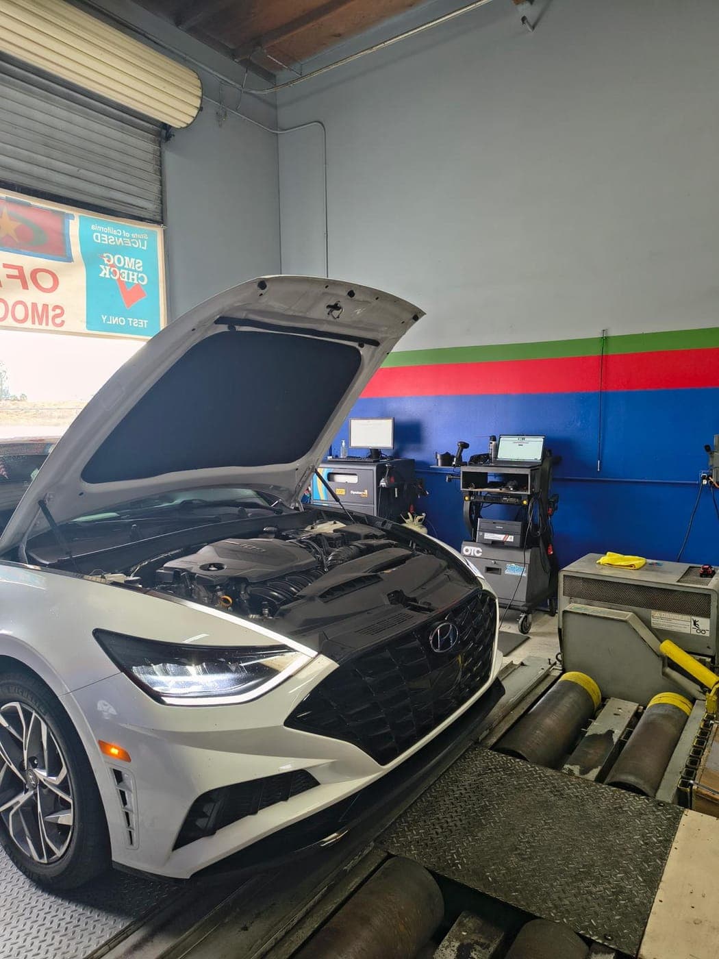 White Hyundai Sonata on the dyno with the hood up, next to the emissions analyzer