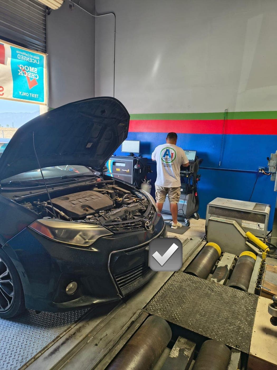 A1 technician in a branded shirt running a smog test at the analyzer while a Corolla sits on the rollers